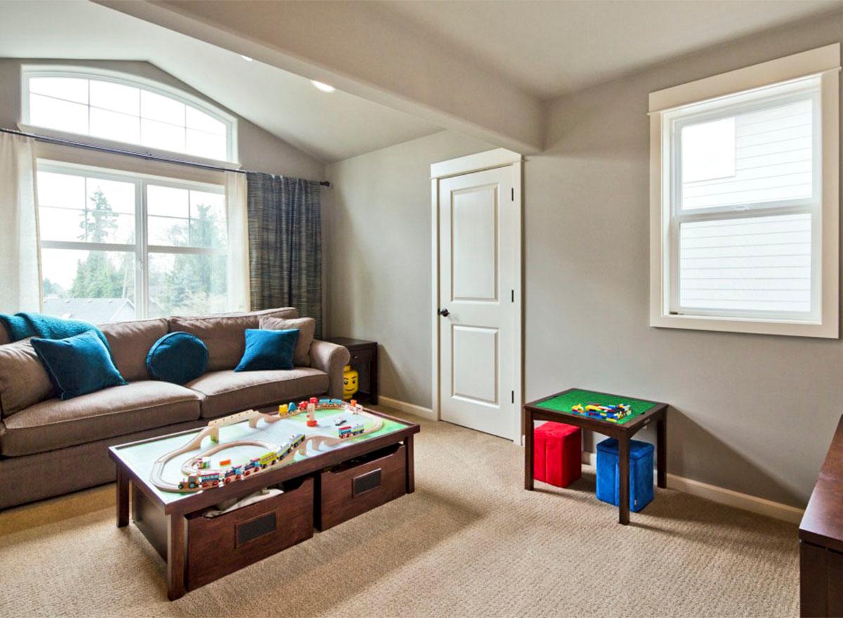 Family room with vaulted ceiling, large windows, sofa, train table, and a dual-pane window.