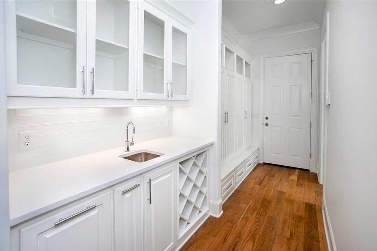Mudroom with white cabinetry, sink, wine rack, built-in bench, and door.
