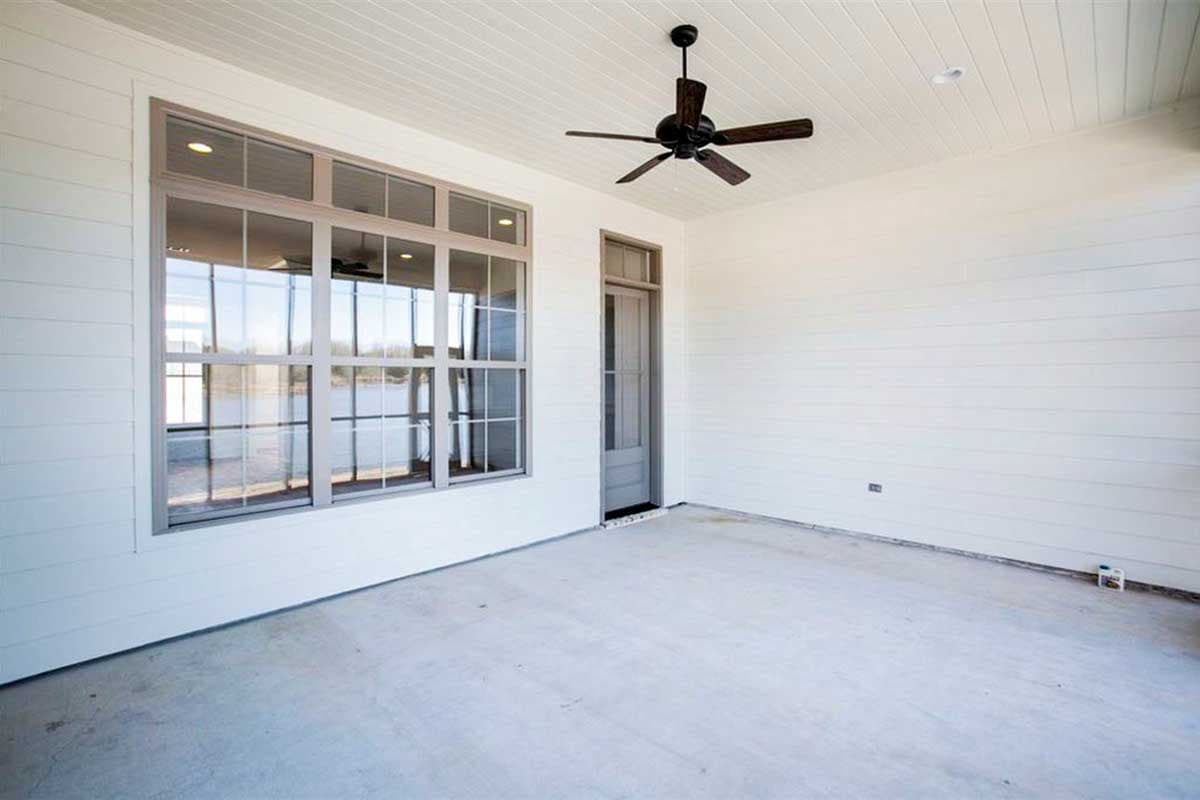 Covered porch with shiplap walls, a ceiling fan, and large bank of windows.