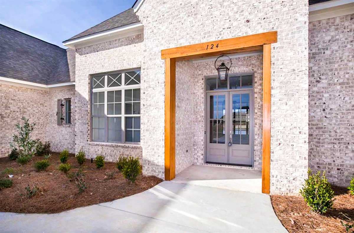 House plan exterior with white brick, double entry doors, large window with cross panes, and wood beam entryway.