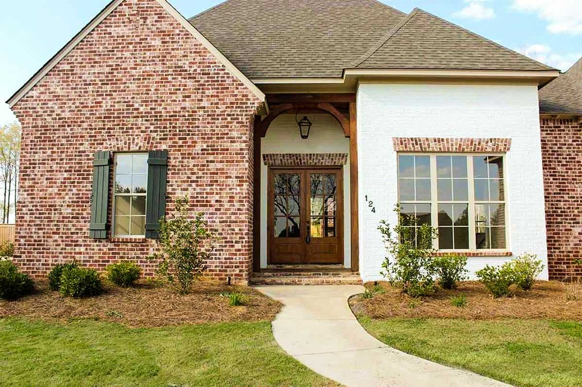 House plan exterior with red brick facade, white painted section, arched entry with double doors, covered porch, and large windows.