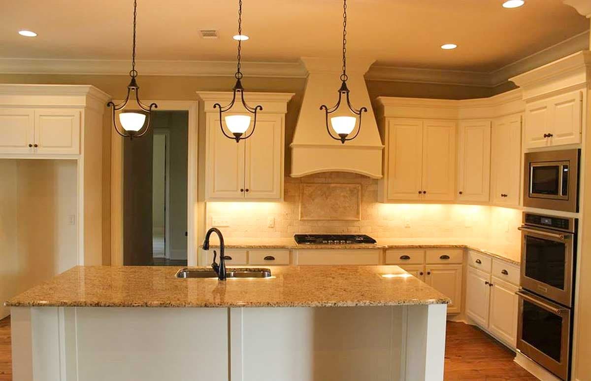 Kitchen interior with island, granite countertops, decorative range hood, white cabinets, and stainless steel appliances.