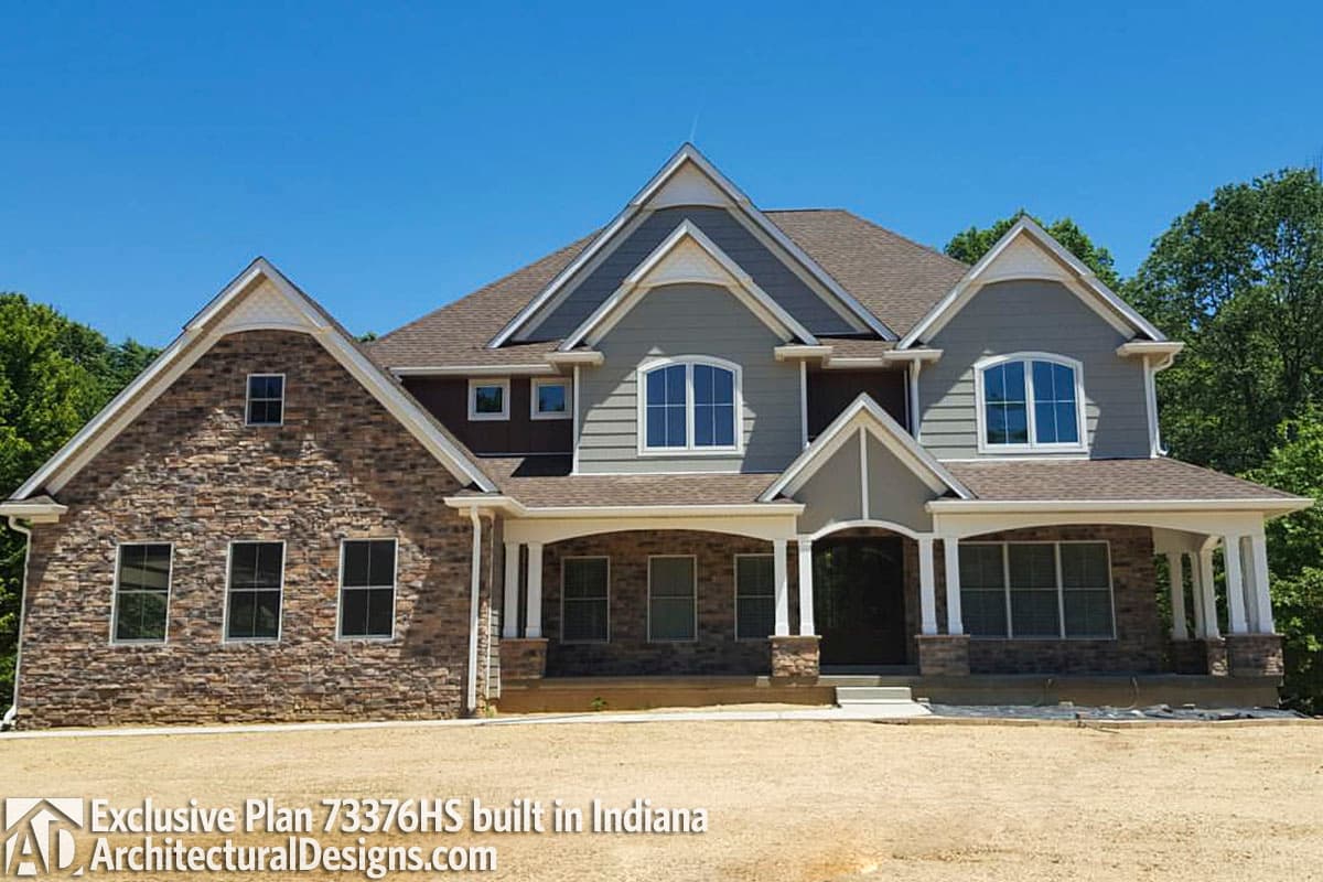 House plan exterior: Two-story home with stone and siding, multiple gables, arched windows, and covered porch.