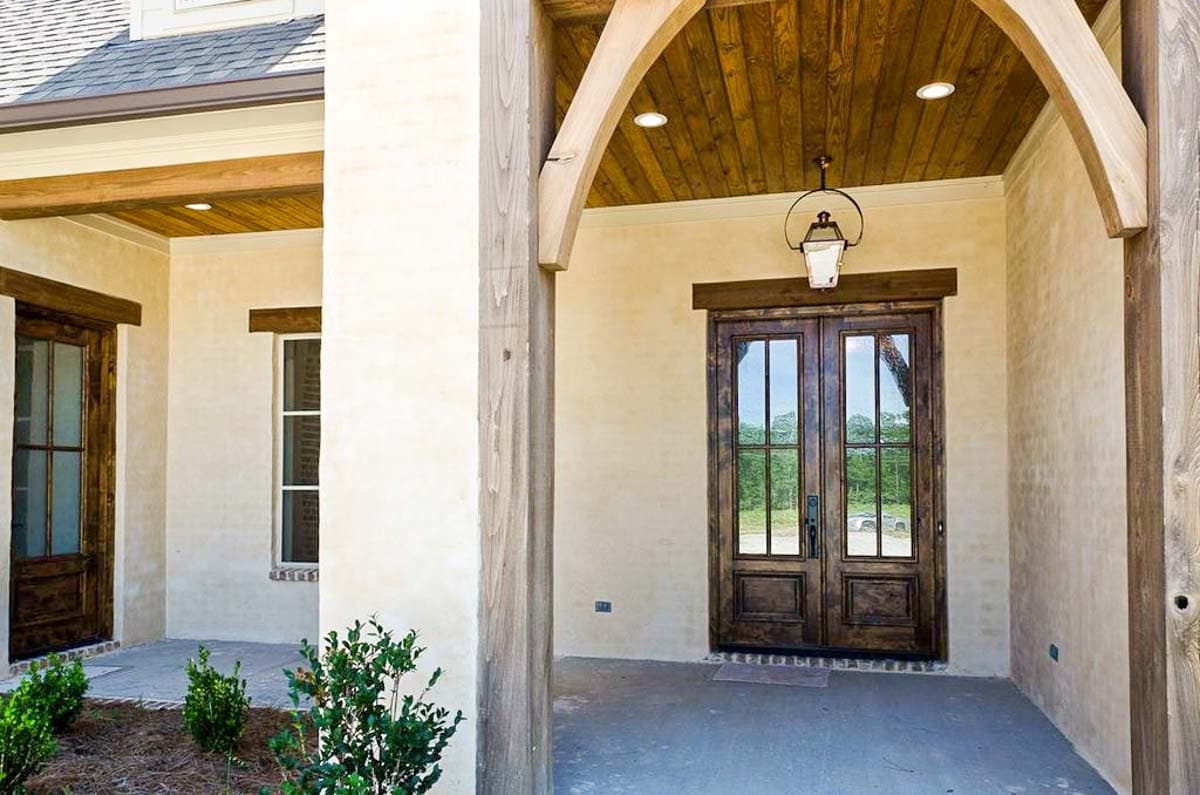 House plan exterior with double wood doors, arched wooden porch beams, wood plank ceiling, and stucco walls.