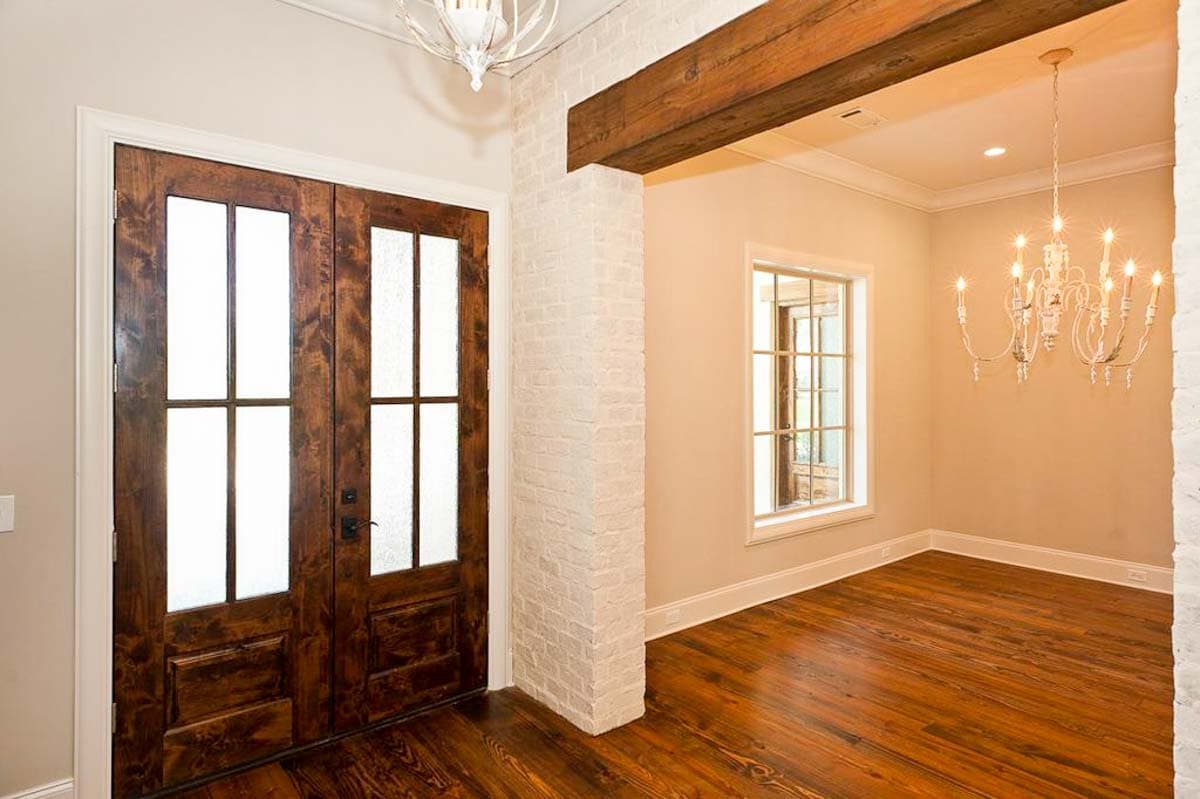 Interior view: Double wooden doors with glass panes, exposed wooden beam, white brick column, and chandelier.