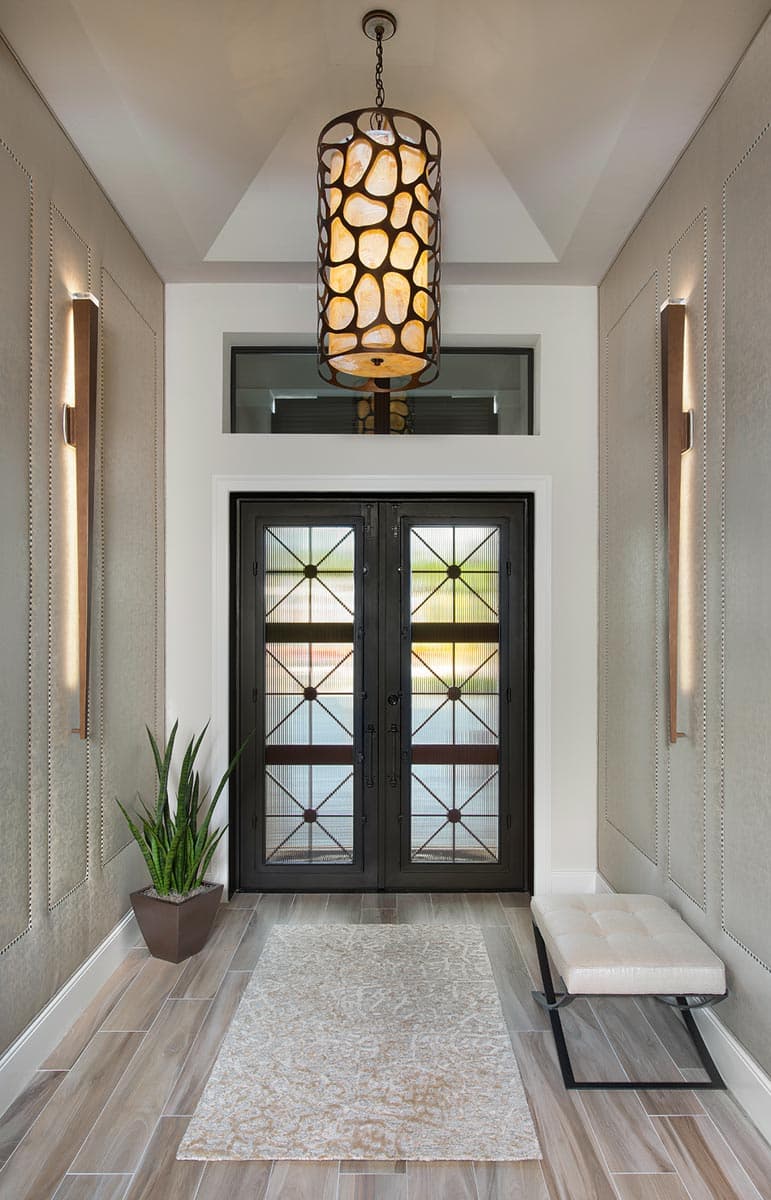 Entryway featuring double glass doors with decorative metal grilles, a patterned pendant light, and wall sconces.