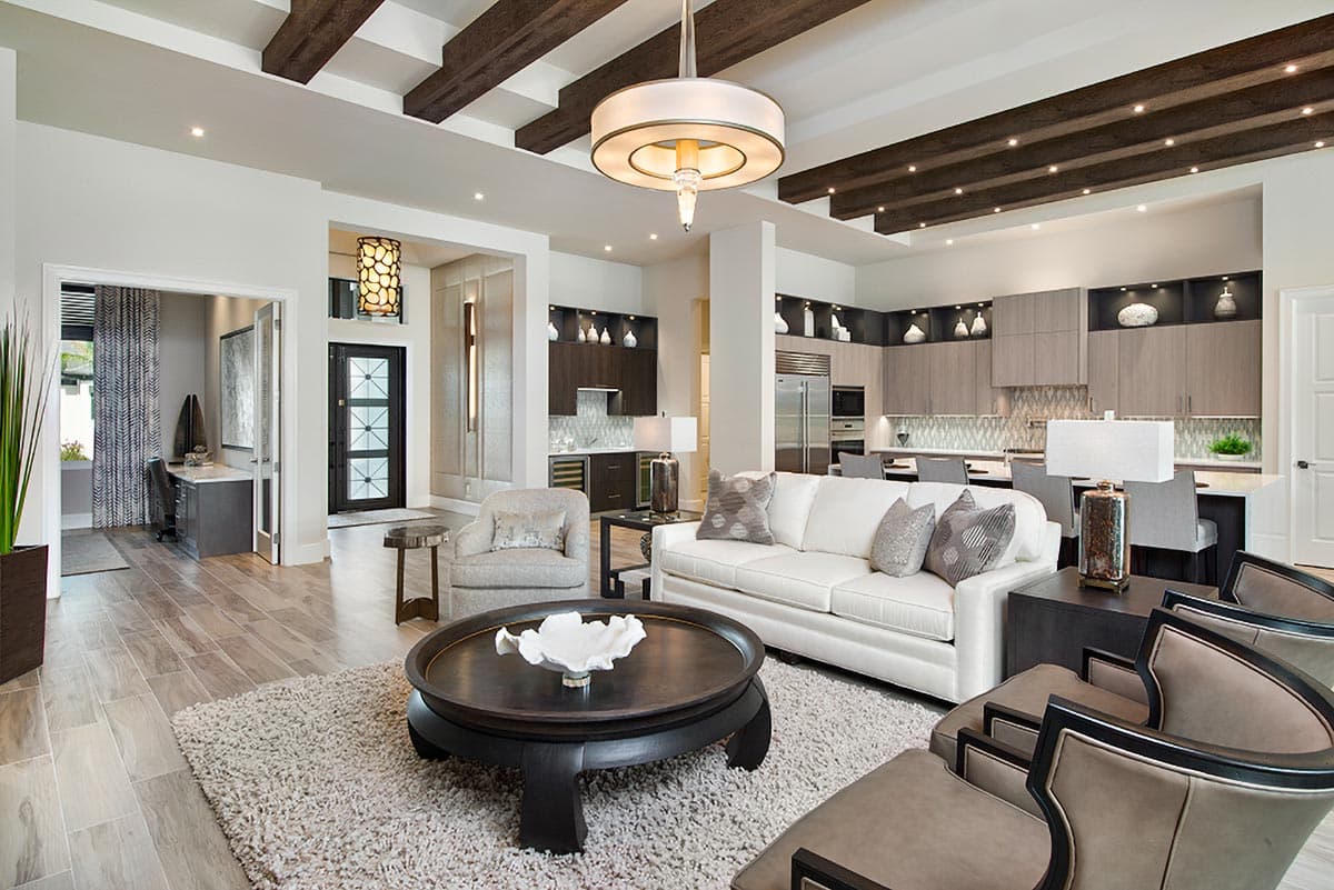 Open-concept living area and kitchen with vaulted beamed ceiling, modern cabinetry, large sofa, and separate office nook.