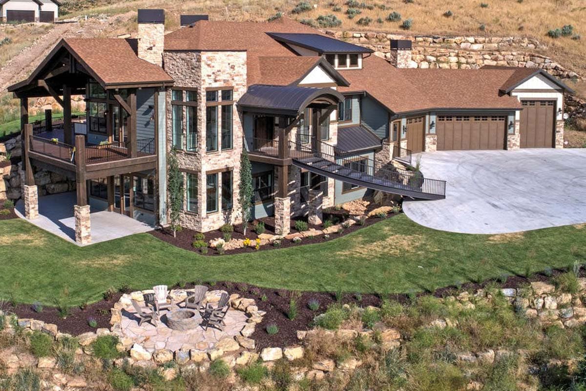 House plan exterior with stone and wood facade, multiple gables, covered decks, and attached three-car garage.