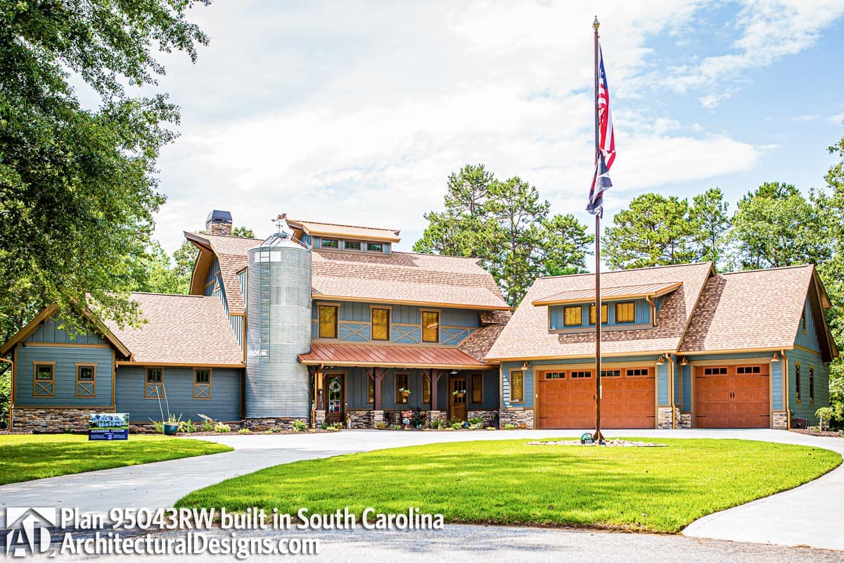 House plan exterior featuring a prominent silo, gabled dormers, metal roof accents, and a three-car garage.