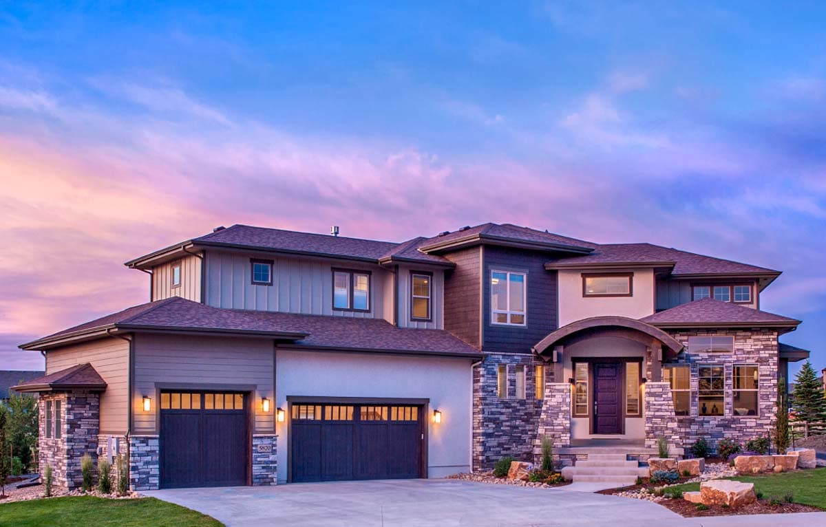 House plan exterior. Two-story home with stone accents, a covered entry, and multiple gabled rooflines. Features two attached garages.