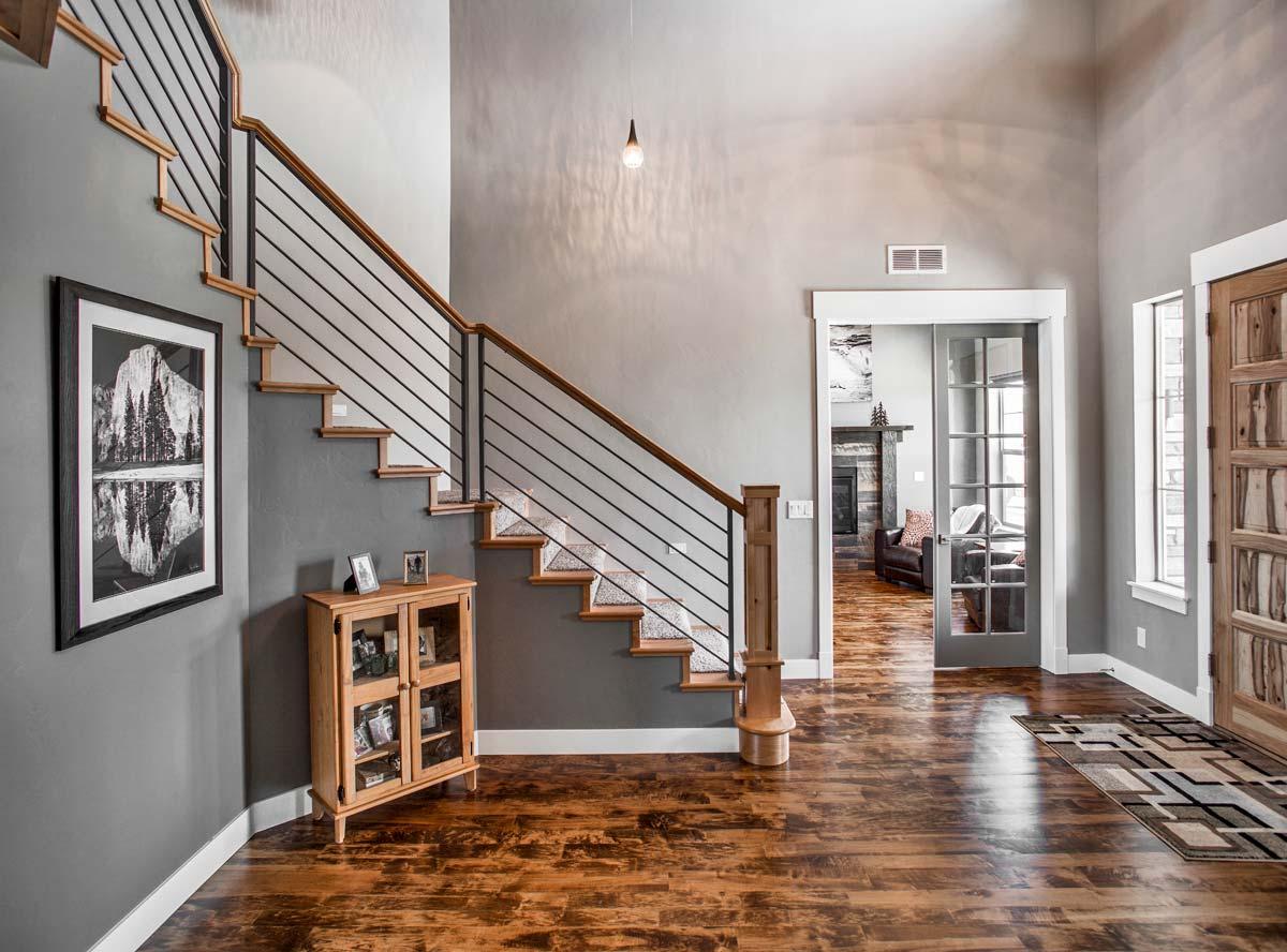 Interior view of a home foyer with a wooden staircase featuring black metal railings, a glass-paned door to a living area, and wood flooring.