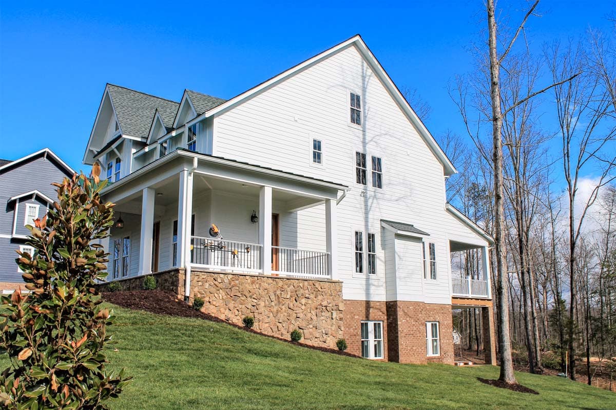 House plan exterior: White siding, gabled dormers, stone foundation, and a wrap-around porch with columns.