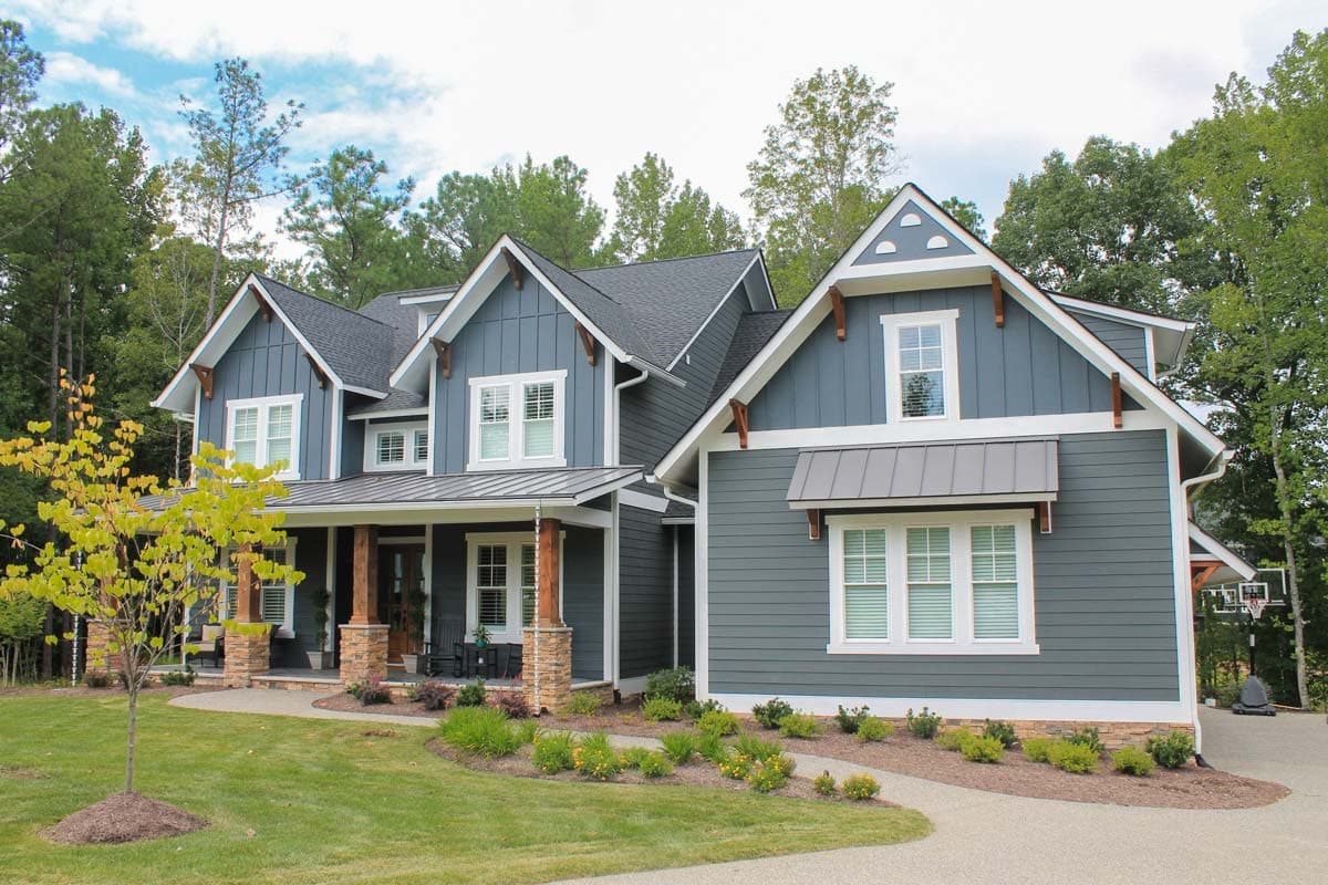 Craftsman style house plan exterior. Two stories, gabled dormers, large front porch with stone pillars, and vertical siding.