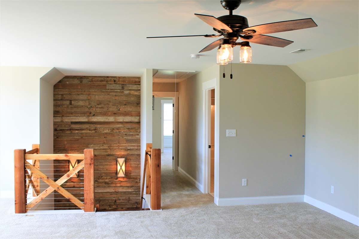 Interior view of a hallway with a wooden accent wall, wood railing, and a ceiling fan. Doors open to other rooms.