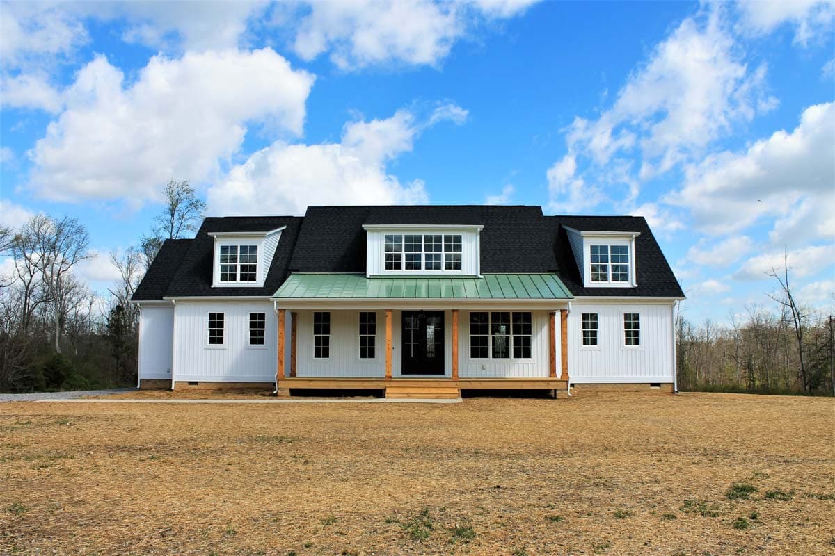House plan exterior: one-and-a-half story home with a covered porch, dormers, and a green metal roof.