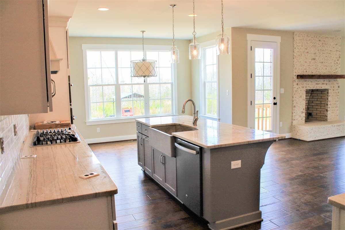 Kitchen with island, farmhouse sink, gas range, and adjacent living area with brick fireplace and glass door.