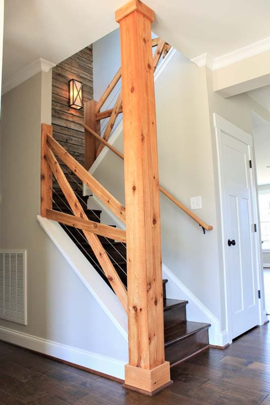 Interior staircase with natural wood newel post, cable railing, and wood plank accent wall with lantern.