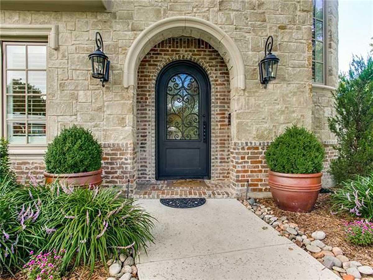 House plan exterior with arched entryway, stone and brick facade, and decorative metal door.