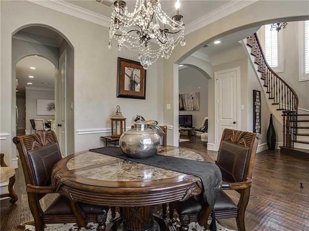 Interior view showing dining area with round table and upholstered chairs, arched entryways, and curved staircase.