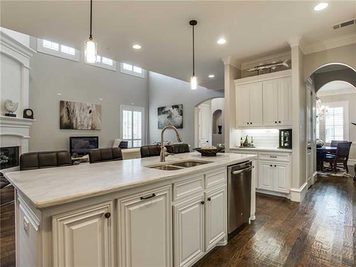 Open concept kitchen with large island, white cabinetry, stainless steel dishwasher, and view into dining room.