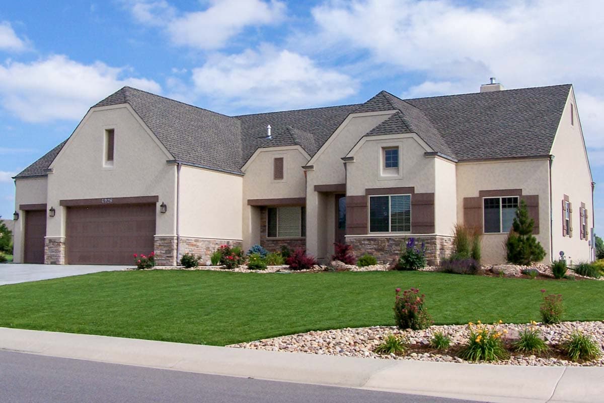 House plan exterior featuring a stucco finish, a three-car garage, varied gables, and stone accents.