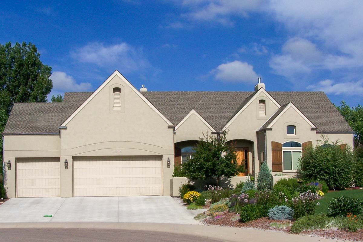 House plan exterior with stucco siding, two-story design, multiple gables, a front-facing garage, and dormers.