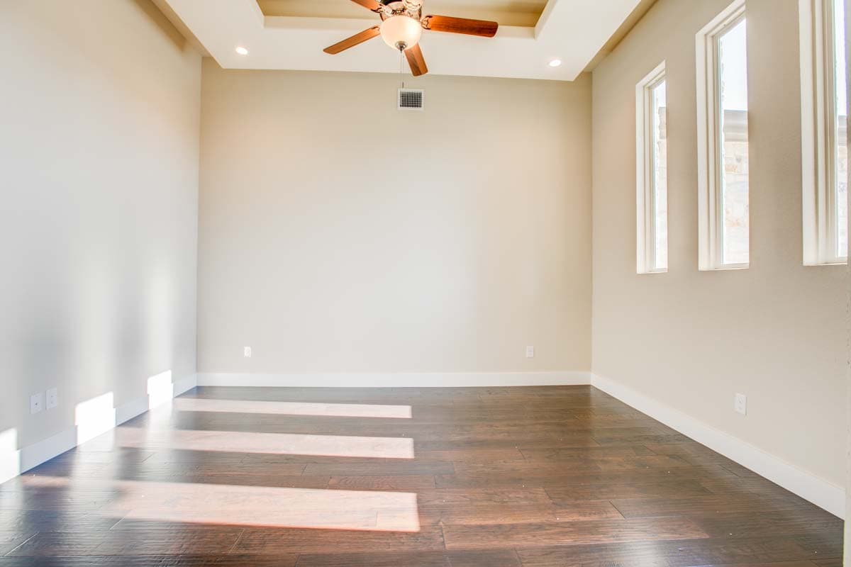 Interior view of an empty room featuring dark hardwood floors, a coffered ceiling with a fan, and three tall, narrow windows.