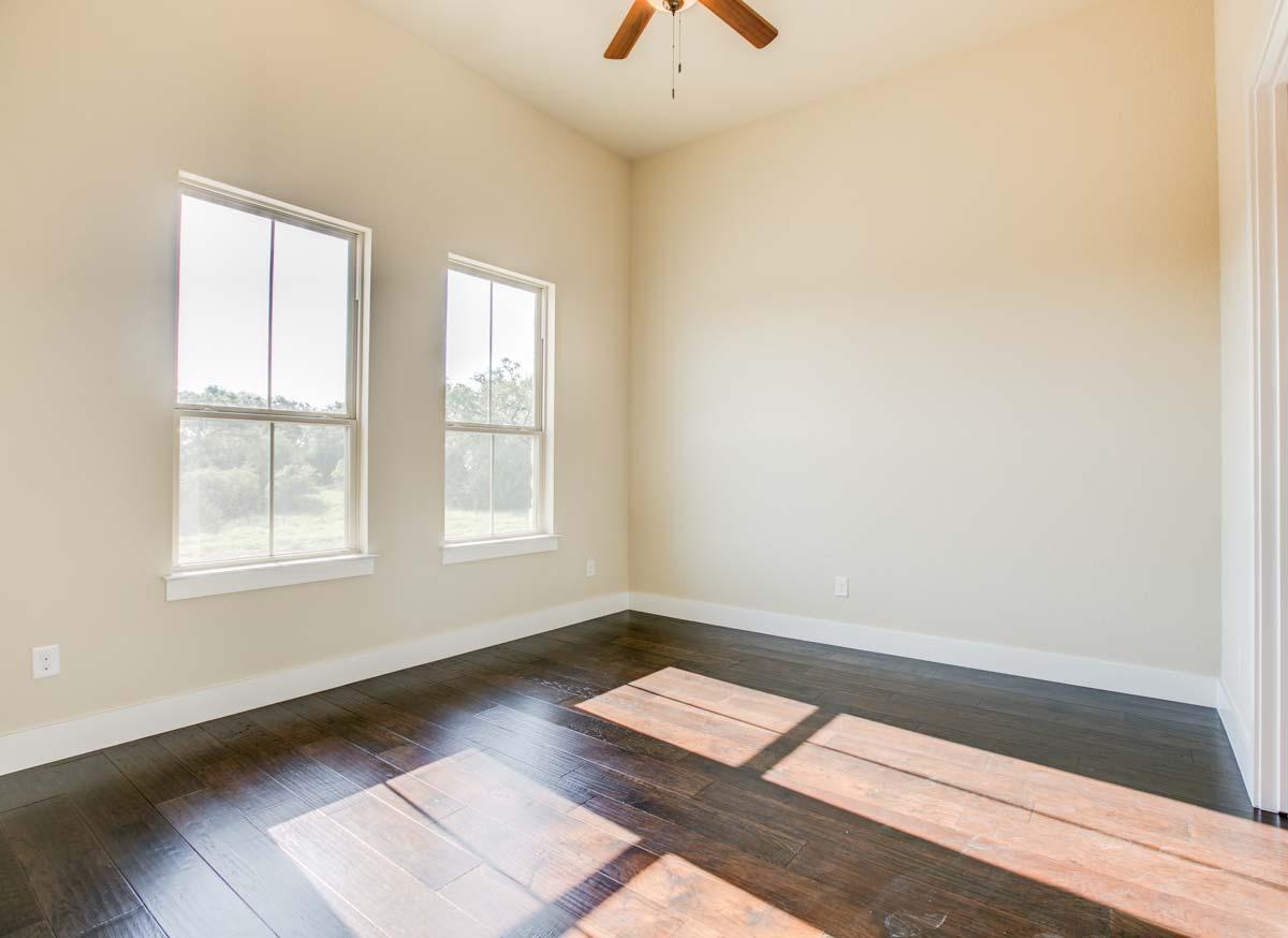 Interior view of an empty room with two tall windows, dark hardwood floors, and a vaulted ceiling with a fan.