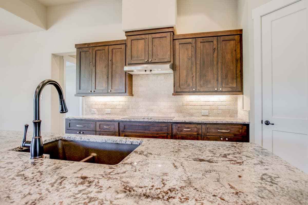 Kitchen interior with dark wood cabinets, granite countertops, a large sink with gooseneck faucet, and stainless steel range hood.