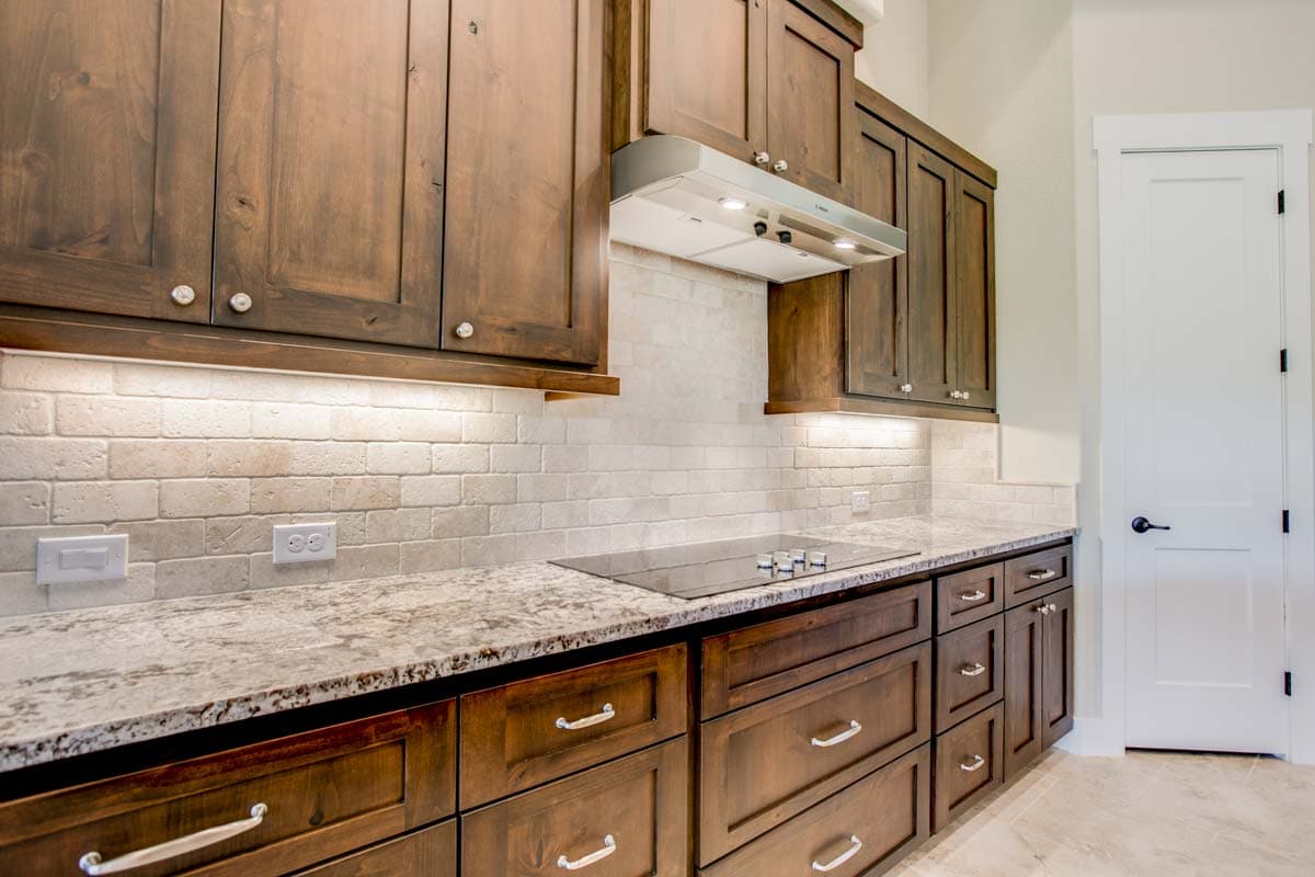 Kitchen interior with dark wood cabinets, granite countertops, tiled backsplash, electric cooktop, and white door.