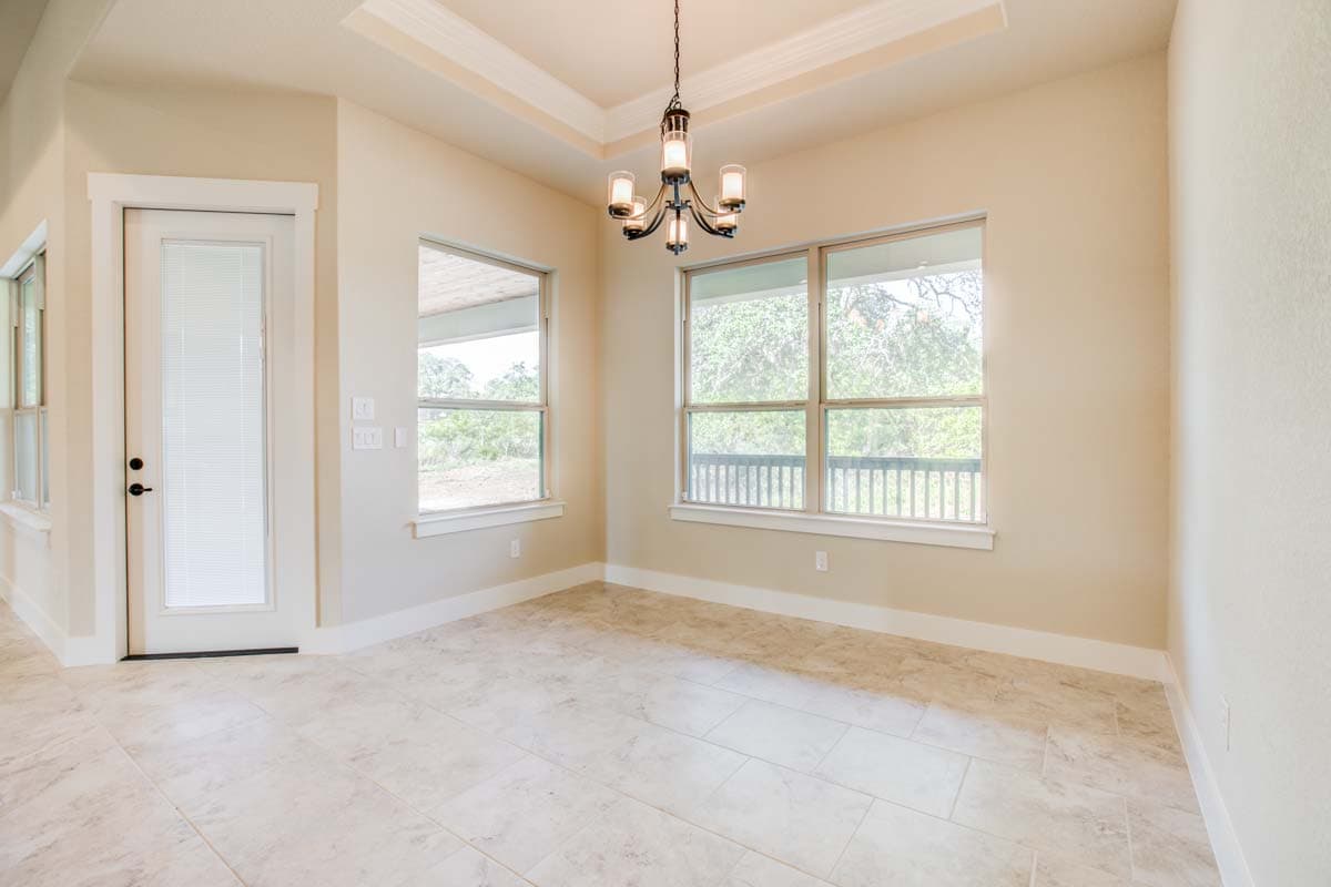 Interior view of dining area with tray ceiling, door to outside, and large windows overlooking a deck.