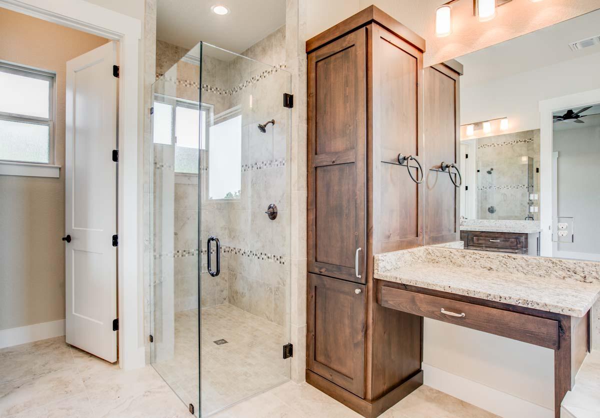 Bathroom with glass-enclosed shower with tiled walls and floor, wooden vanity with granite countertop, and white door.