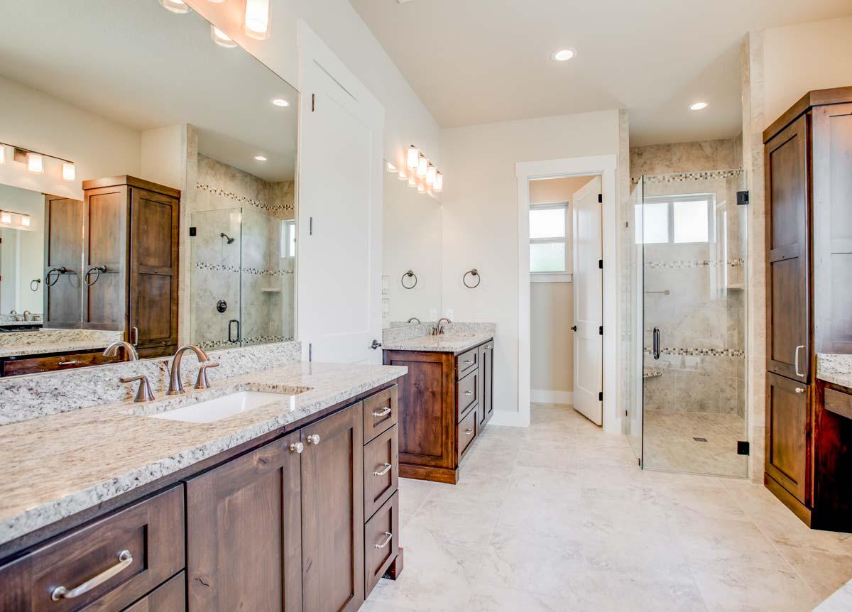 Spacious bathroom with double vanity, granite countertops, walk-in shower with glass door, and dark wood cabinetry.