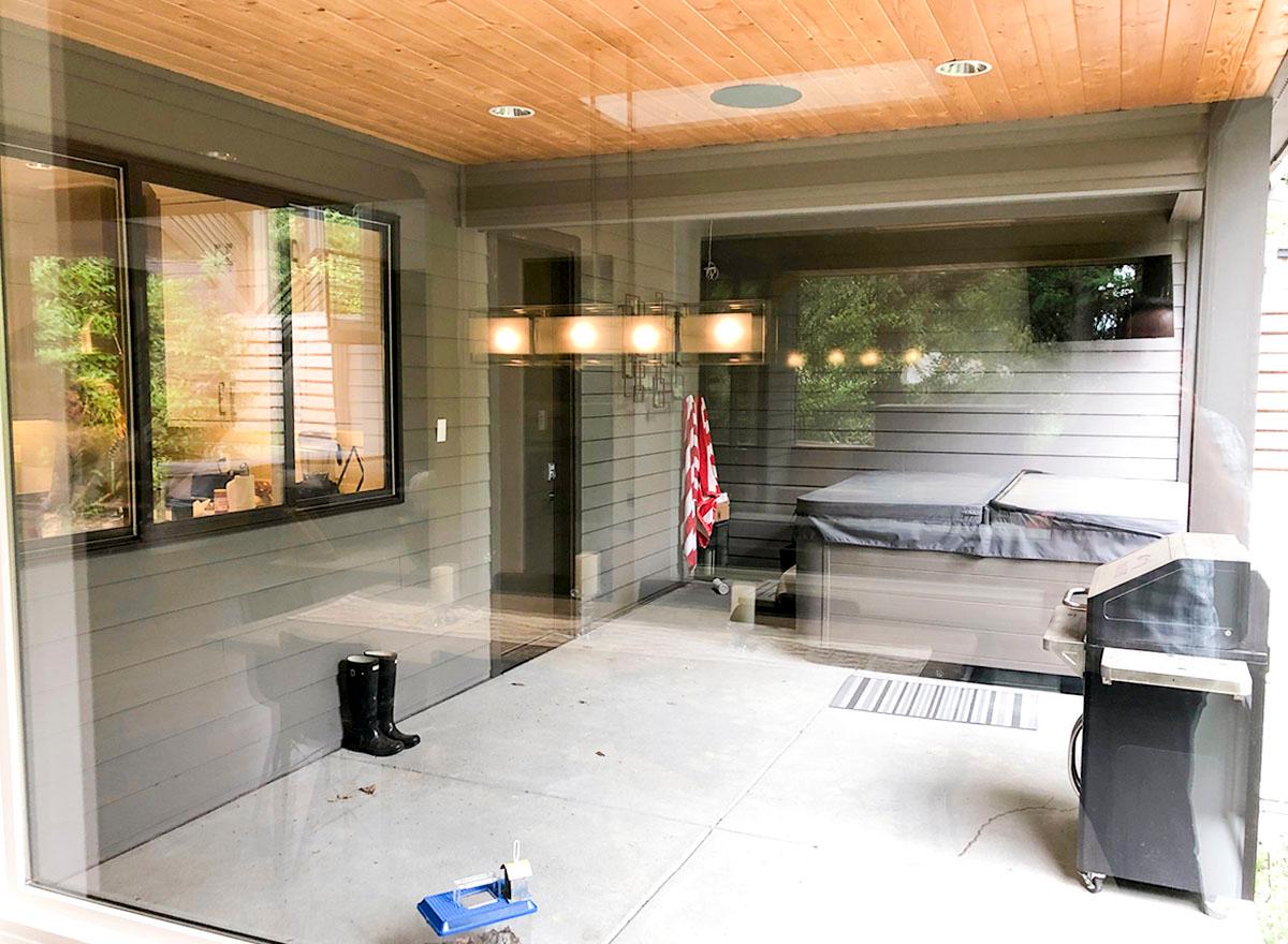 Covered patio with wood ceiling, hot tub, grill, and large windows.