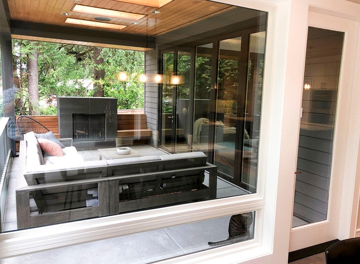 Covered patio with fireplace, sectional sofa, and coffee table, viewed through glass doors.