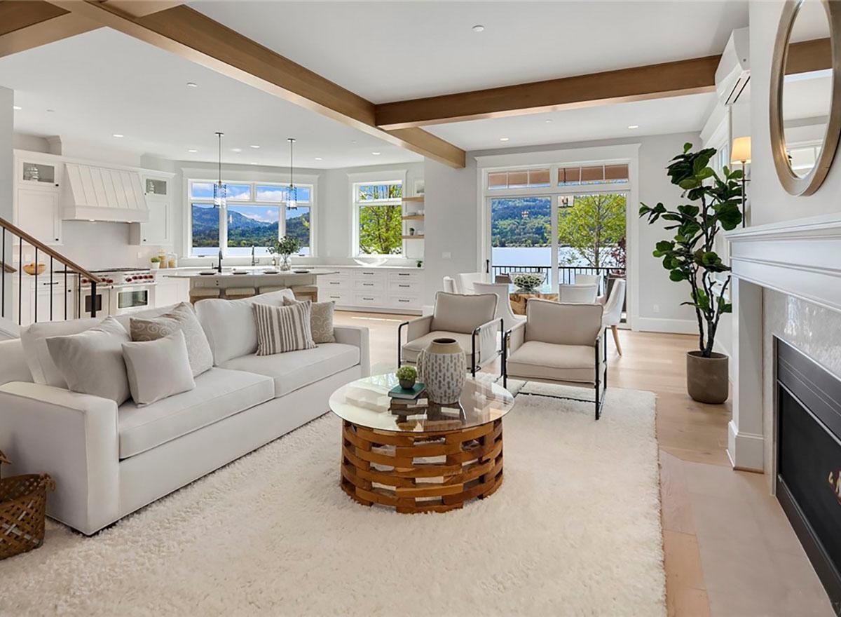 Open concept living area with kitchen, dining, and living rooms featuring vaulted ceilings, exposed beams, and large windows overlooking a lake.