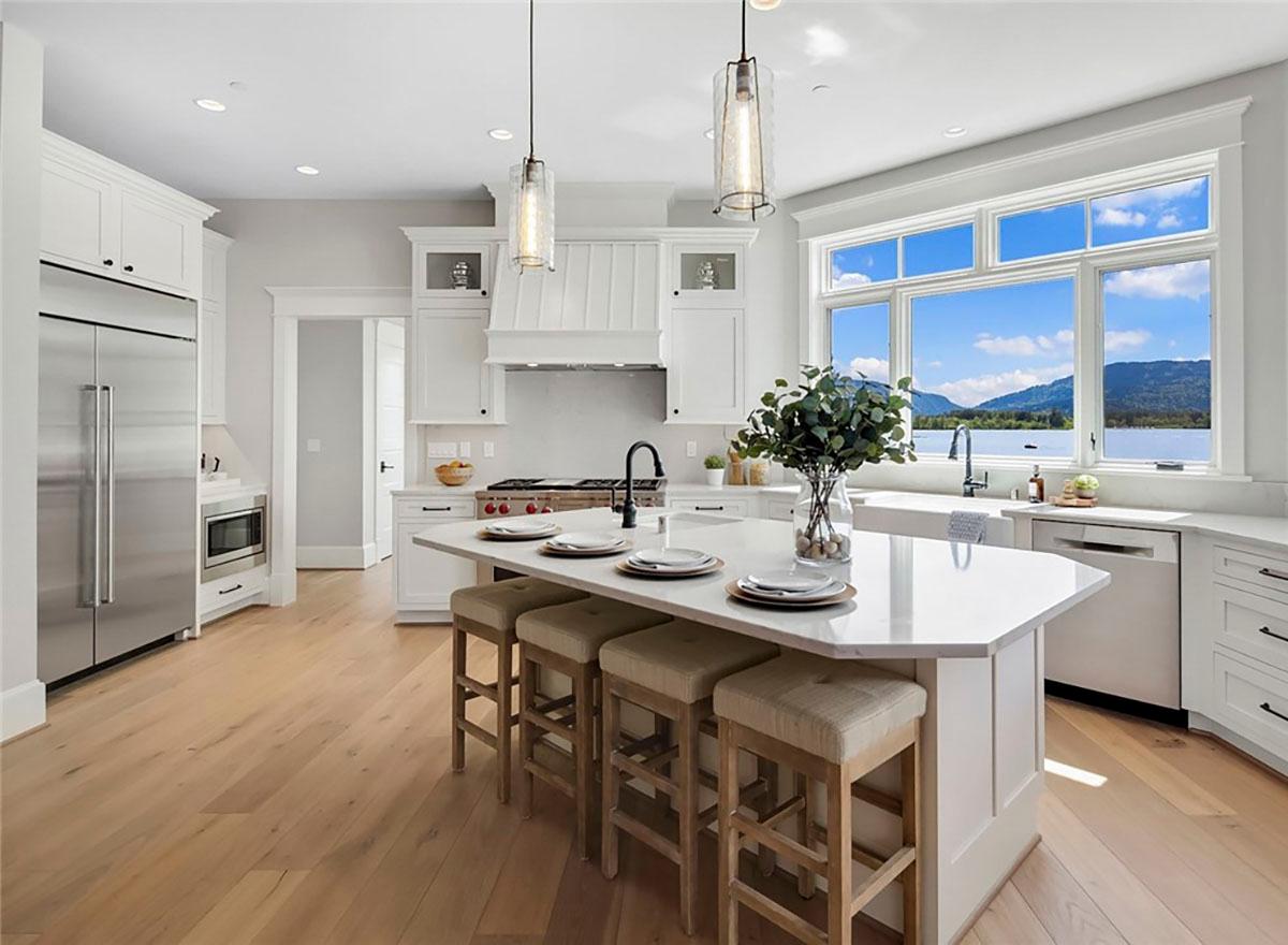 Contemporary kitchen with white cabinetry, large island with seating, stainless steel appliances, and a sink with a large window view.