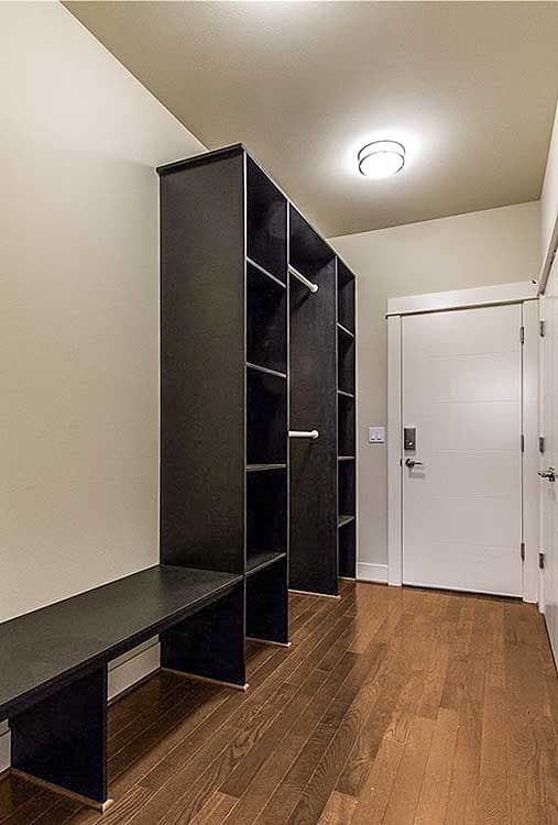 Walk-in closet with dark wood shelving, integrated bench, hardwood floors, and flush panel doors.