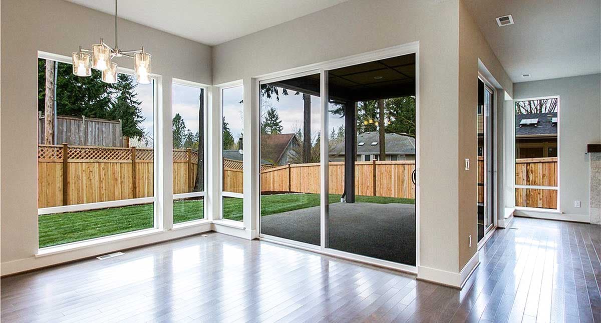 Interior view of a room with large windows, sliding glass doors to a covered patio, and hardwood floors.