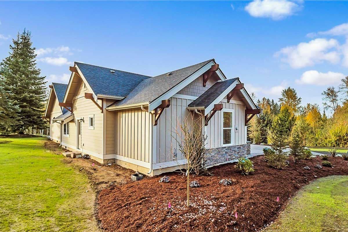 House plan exterior with multiple gables, decorative rafter tails, lap siding, and stone skirt.