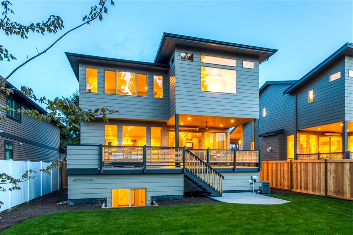 Modern two-story house plan exterior with a covered deck, horizontal siding, and numerous windows.
