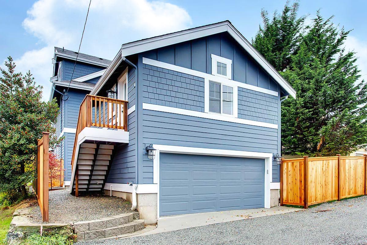 House plan exterior with two stories, gabled roof, and attached garage. Exterior features include a balcony with wooden railing, and shake siding.
