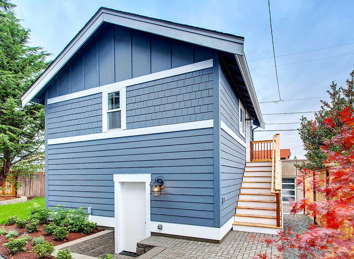 House plan exterior with blue siding, shingled upper section, prominent gables, and wooden exterior stairs.