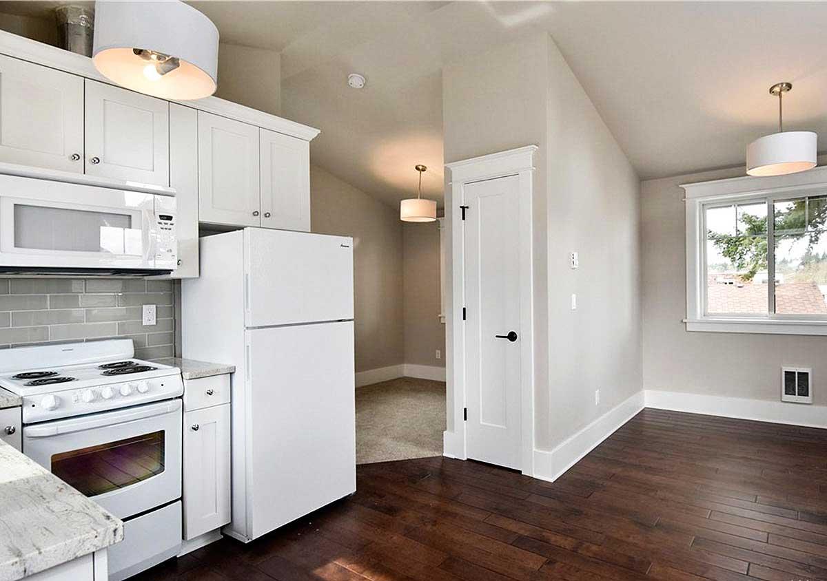 Interior view of a small kitchen with white appliances, cabinets, subway tile backsplash, and adjacent doorway to another room.