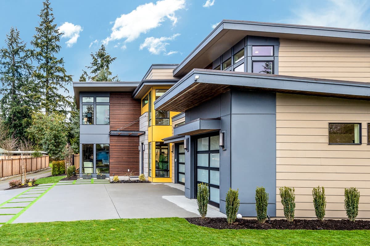 Modern house plan exterior with angled rooflines, multi-level sections, wood and composite siding, and glass garage doors.