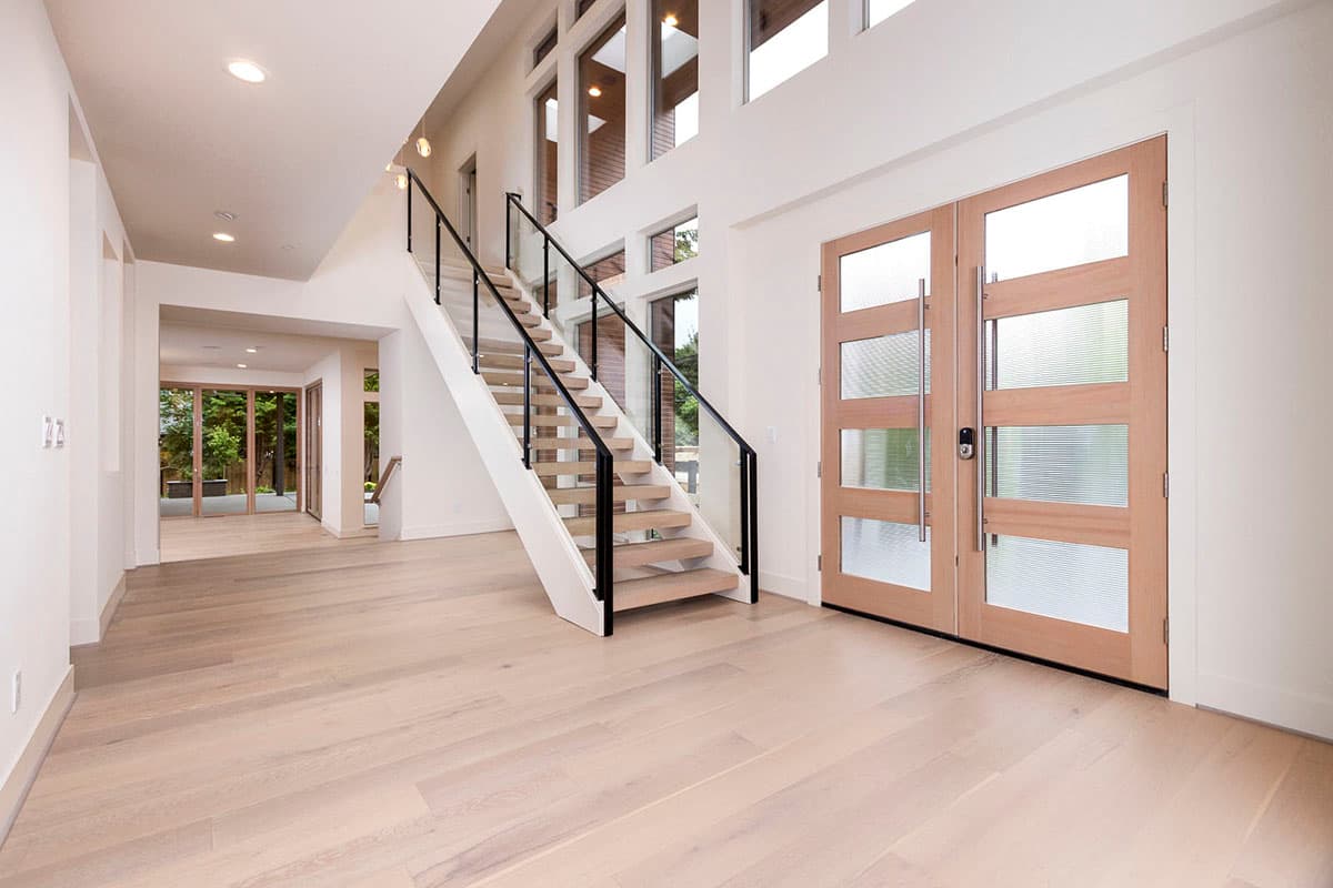 Modern home interior with open staircase, double glass doors, and a wall of windows.