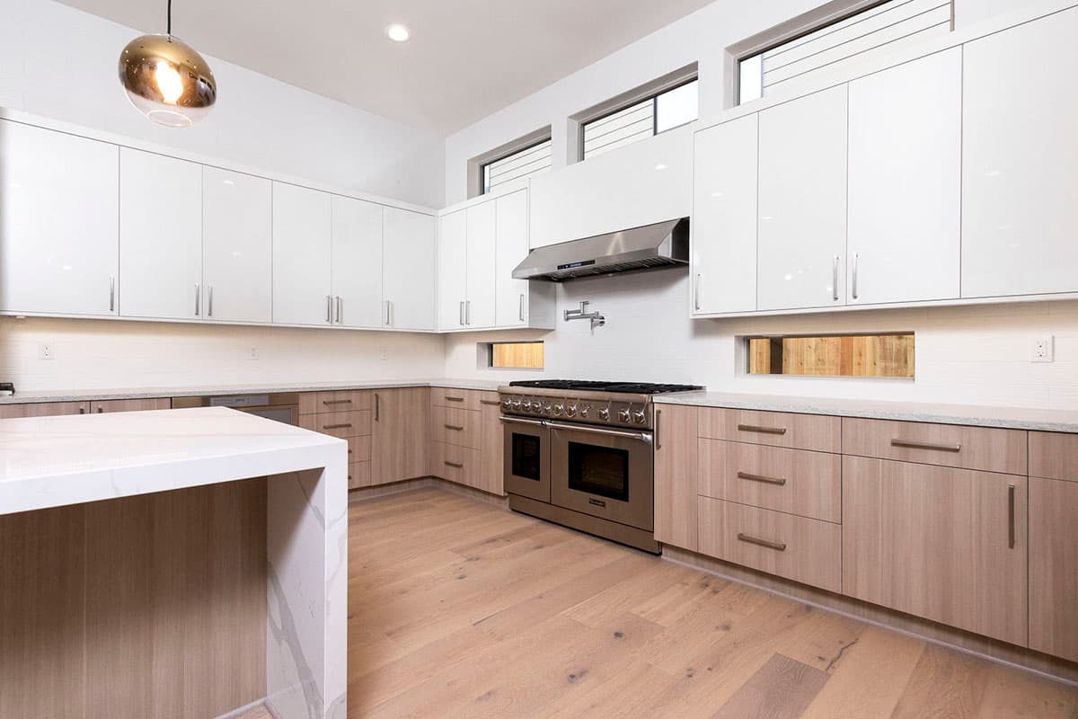 Modern kitchen with white upper cabinets, wood lower cabinets, stainless steel range and hood, and a marble island.