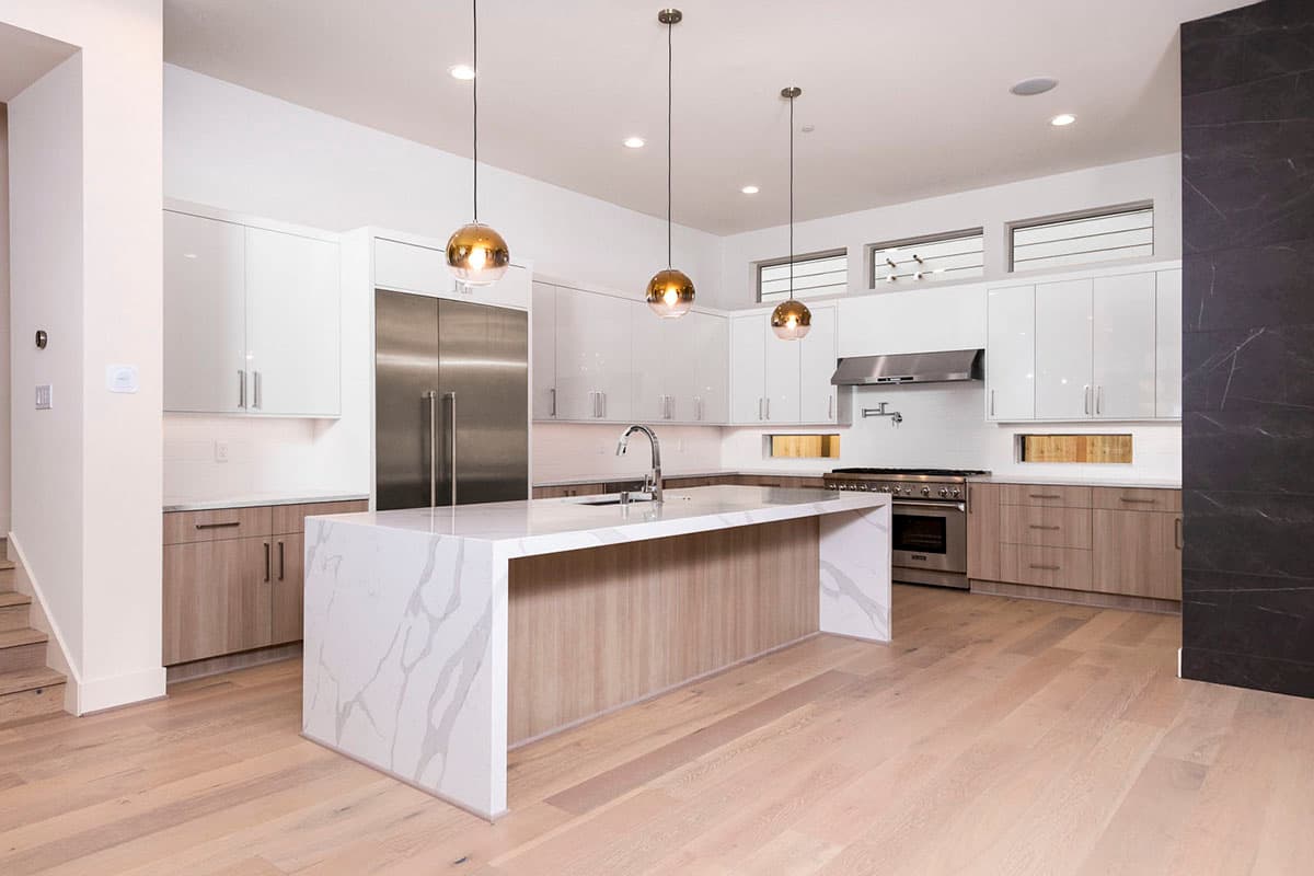 Modern kitchen with waterfall island, stainless steel appliances, sleek white cabinetry, and natural wood lower cabinets.