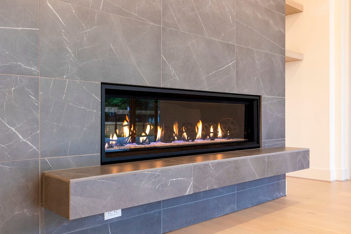 Modern linear gas fireplace with gray marble tile surround and floating hearth.