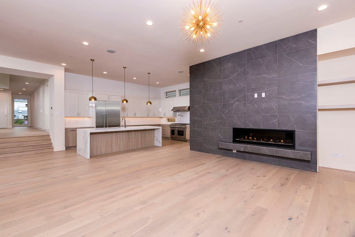 Modern open-concept living area with kitchen island, sleek cabinetry, and linear gas fireplace.